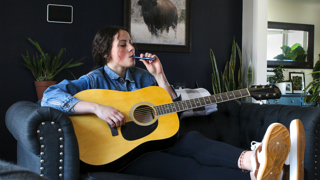 Woman sitting with a guitar, smoking a discreet THC vape.