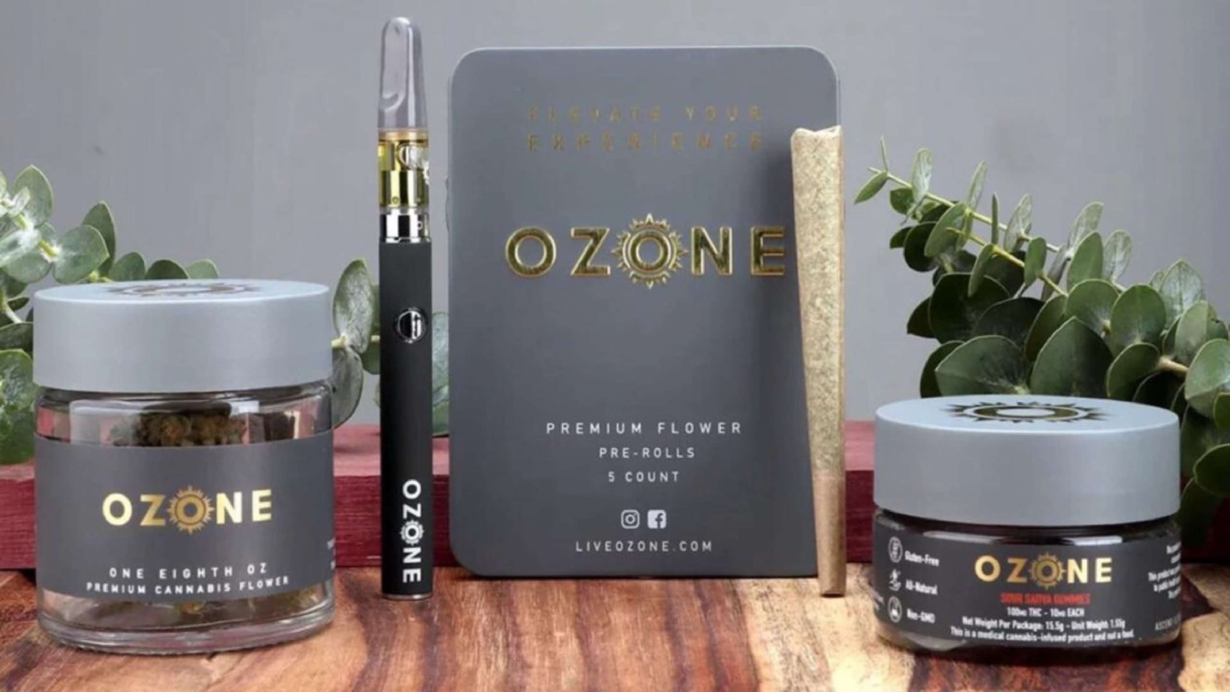 A lineup of Ozone cannabis products, including pre-rolls, gummies, premium flower, and a vape cartridge, displayed against a wooden table with greenery for a natural aesthetic.